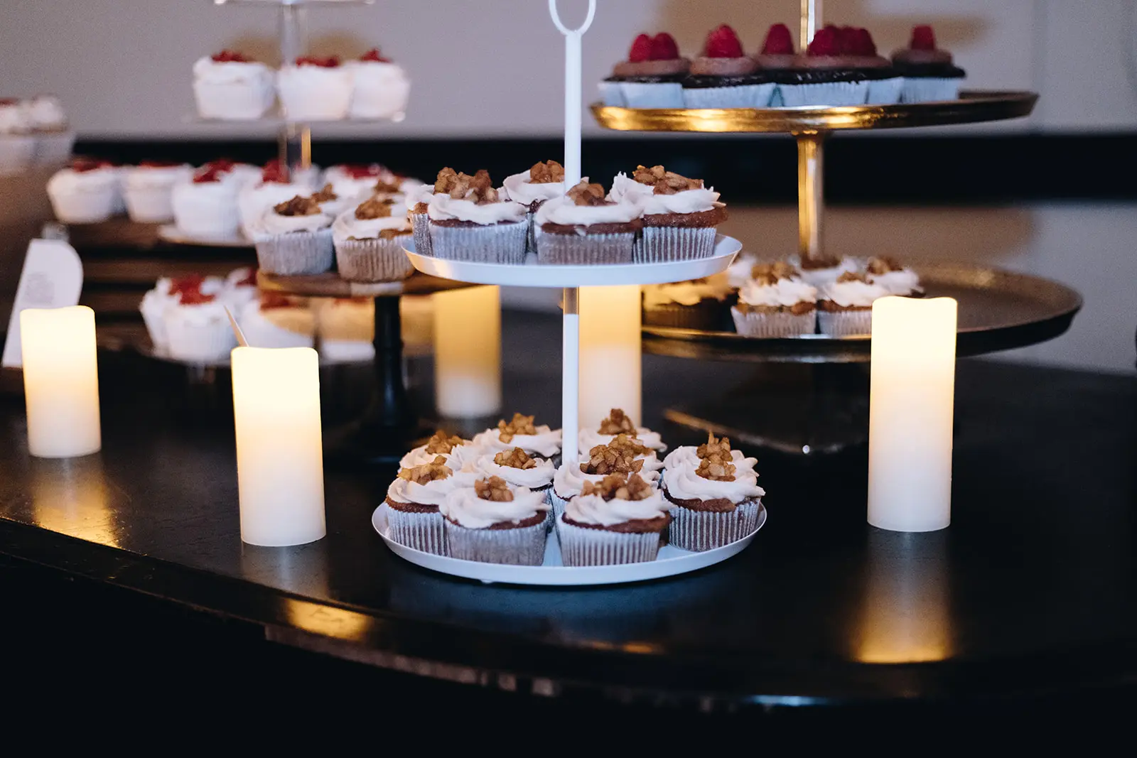 Tiered cupcake stands with candles, part of a dessert station at a reception.
