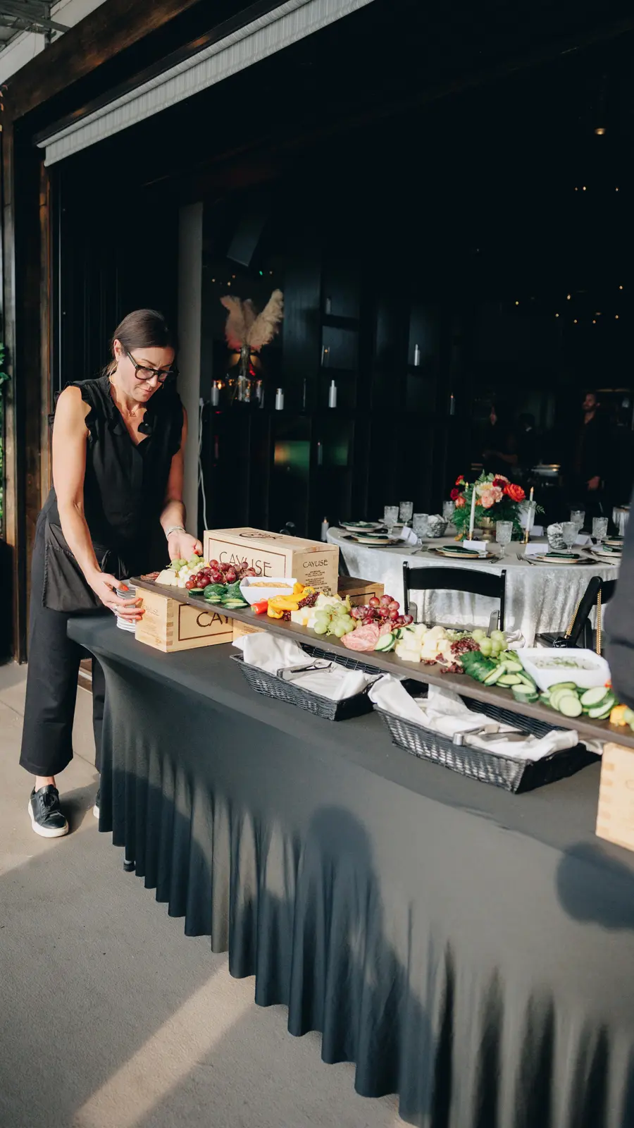 A member of our team laying out a grazing board in the main room, with dinner tables set behind.