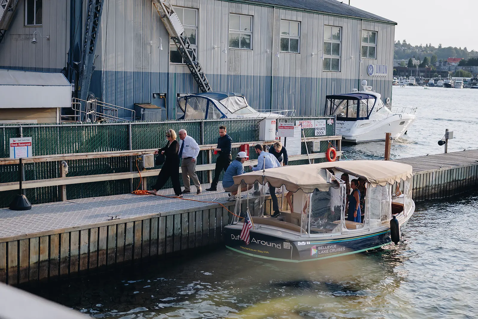 Guests stepping off a covered water shuttle onto the dock, with private boats and Lake Union behind them.
