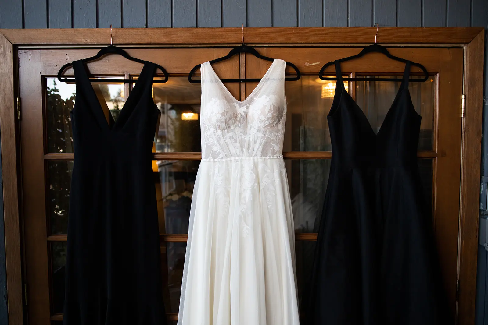 A wedding dress hanging between two black bridesmaid dresses on a wooden door frame.